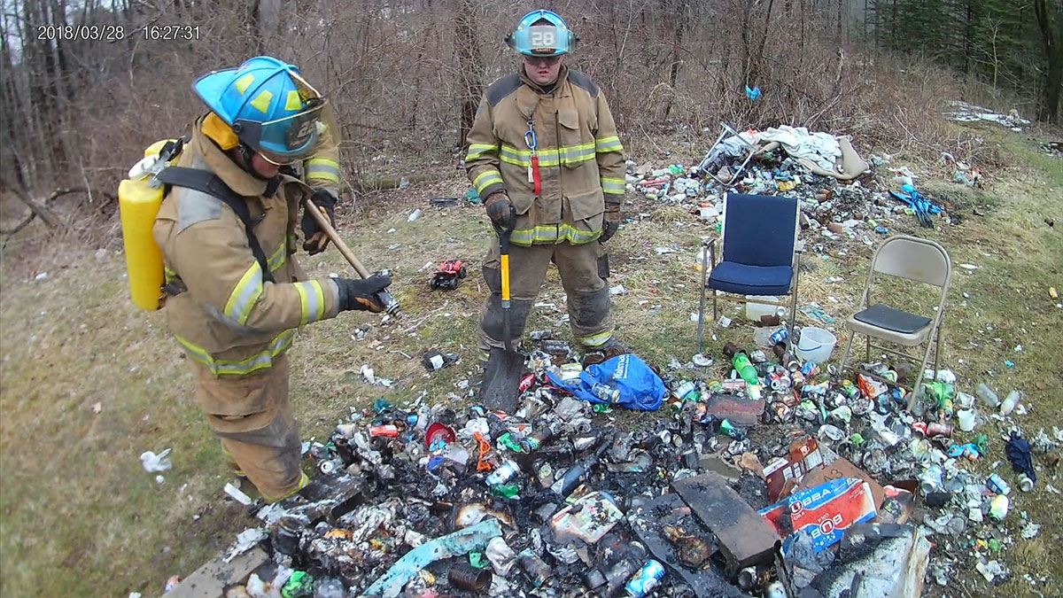 Firefighters Mike Rayburn and Kyle Corey use a portable tank and hand tools to extinguish a trash fire