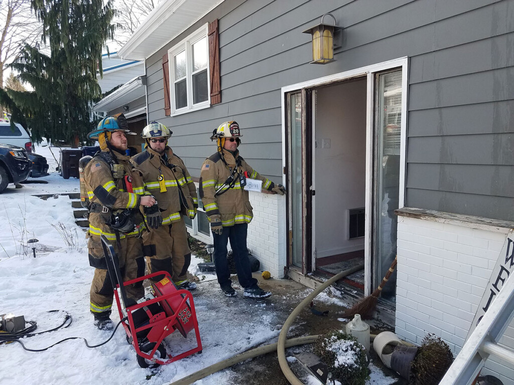 Firefighter Matt Jastromb, Rescue Chief Jayme Corey, and Fire Chief Craig Lauer stand at the front door of a house with a room and contents fire