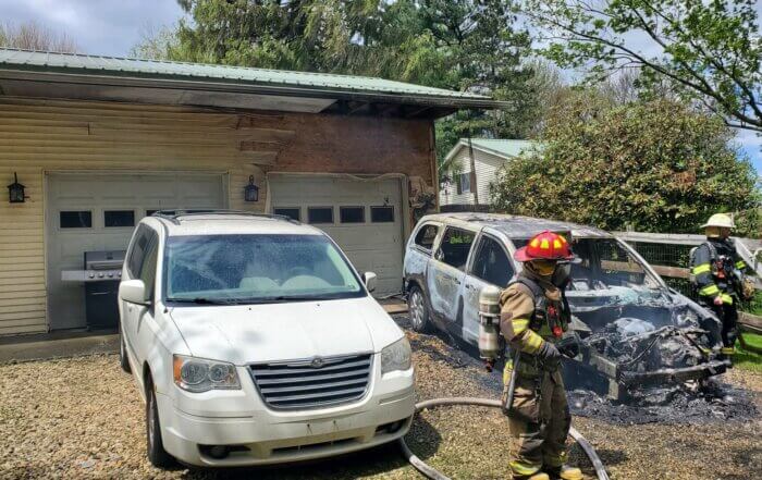 firefighters inspect a vehicle that was recently on fire near a garage